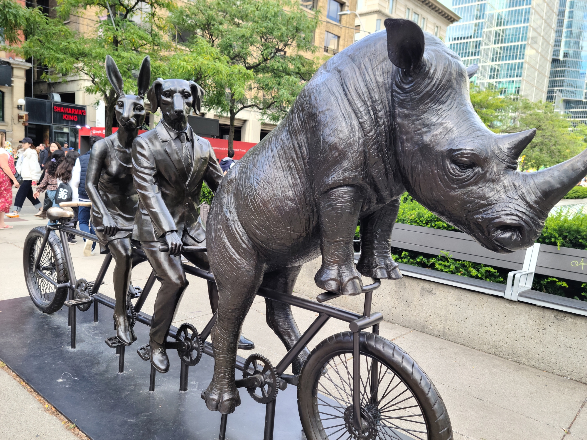 3 human bodies with animal heads riding a 4-seated bike